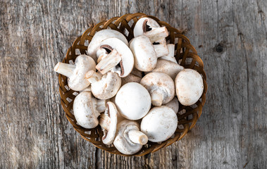 Fresh champignon mushrooms in a basket on wooden table, overhead