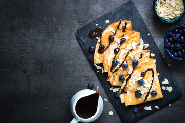 Crepes with blueberries almond flakes and chocolate sauce on black.