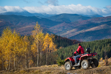 Male on an ATV on the hilly road enjoying mountains, automn forest and blue sky. The concept of an active holiday in the mountains