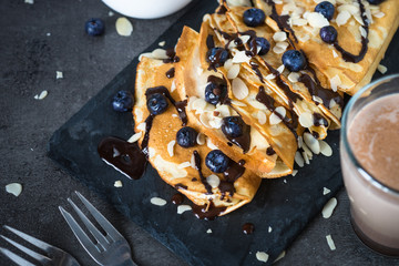 Crepes with blueberries almond flakes and chocolate sauce on black.