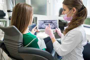 Female dentist and patient examining x-ray picture in dental clinic. Doctor showing thumbs up to...