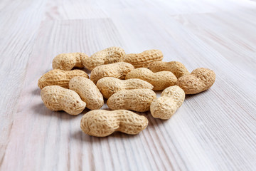 A heap of unpeeled peanuts on a light kitchen table close-up.