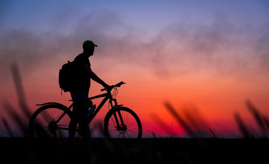 Fototapeta na wymiar Silhouette of cyclist on the background of red sunset. Biker with bicycle on the field during sunrise