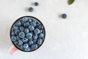 Organic blueberries in a mug for healthy eating on light gray table.