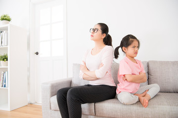 mother and daughter back to back sitting on sofa