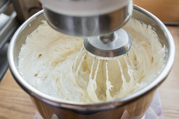 Closeup of electric mixer with whipped smooth dough for cake. Batter being whipped. Mixing white...