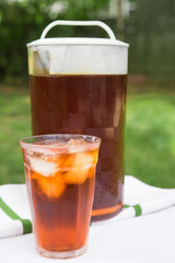A glass of iced tea and pitcher in a backyard summer setting