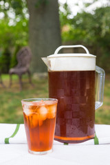 A glass of iced tea and pitcher in a backyard summer setting