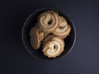 Danish vanilla wreaths cookies (vanillekranse) in black rustic bowl, isolated on black background