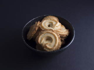 Danish vanilla wreaths cookies (vanillekranse) in black rustic bowl, isolated on black background