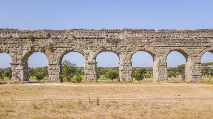 Vista aerea frontale dei resti di un'acquedotto romano situato nel parco degli Acquedotti a Roma, vicino la fermata metro Cinecittà. In primo piano dei campi di grano.