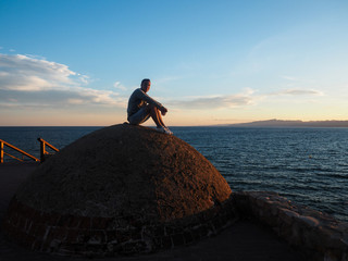 A man sits near the sea at dusk