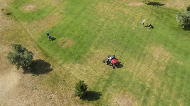 Vista aerea di un gruppo di giardinieri che lavora e cura l'erba. Una macchina, chiamata tosaerba, tosa il prato. Il campo da lavorare è grande e richiede molte cure e attenzioni.
