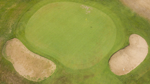 Vista aerea della bandiera gialla e della buca finale di un campo da golf in un centro sportivo a Roma, in Italia. Sullo sfondo due ostacoli formati da una buca di sabbia per complicare il gioco.