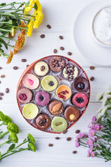 Handmade luxury chocolate candies in a gift box, coffee cappuccino and multicolored chrysanthemums on white wooden background