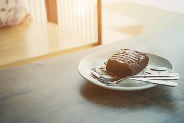Close up of plate with stack of delicious and soft, square sliced chocolate brownies and extra brownies at the pan behind it. Top view image with dark vintage wood background.
