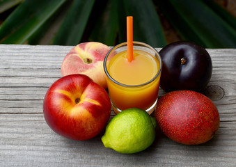 Fresh ripe fruits and a glass of juice in tropical garden.Multi fruit juice.Juice mix fruit on wooden table.Healthy drink or diet concept.Selective focus.