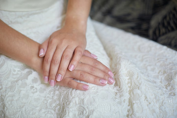 Hands of the bride with a manicure on a white dress