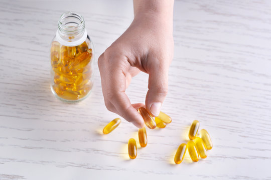 Woman Holding Fish Oil Capsule In Hand Over Table