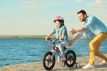 Young man teaching his daughter to ride bicycle outdoors near river