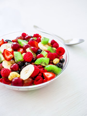 Fresh salad with fruits and berries in glass bowl on white table.