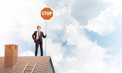 Caucasian businessman on brick house roof showing stop road sign. Mixed media
