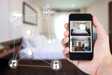 Hand holding smartphone view looking in house on blurred house background with Home security CCTV system concept.