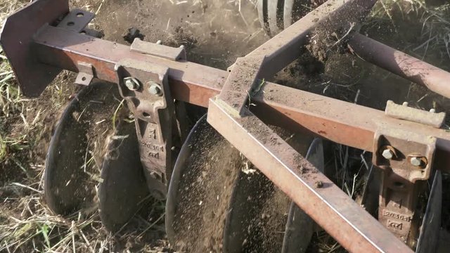 Closeup of plow attached to a tractor plowing a field.