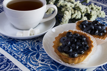 Cake with blueberries, tea and flowers on the blue tablecloth