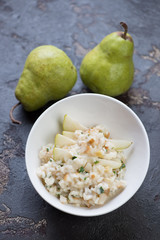 White bowl with pear risotto on a brown stone background, vertical shot, selective focus