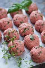 Close-up of fresh uncooked meatballs with seasonings on a baking paper, selective focus, shallow depth of field