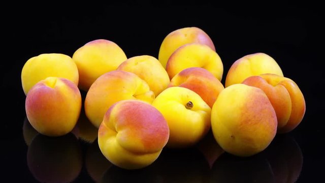 Excellent side view close up of fresh red and yellow apricots, Prunus armeniaca, laying on black surface with reflection and rotating clockwise. Vibrant flat lay of yummy dessert with amazing texture.