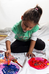 Little girl sitting down and playing with color paint