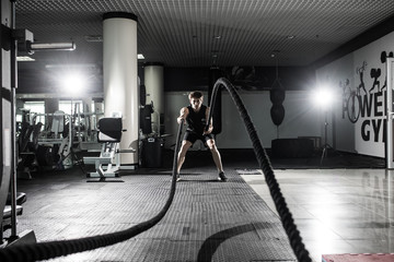 Strong Men with battle rope battle ropes exercise in the fitness gym. CrossFit.