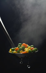 Boiled green peas, corn and carrot in a ladle with steam on a dark blue background. © YuryGulakov