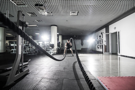 Athletic man doing some cross-training exercises with a rope in gym. Crossfit