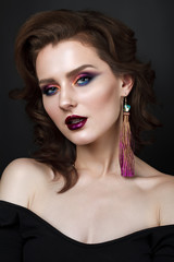 Portrait of beautiful young woman with professional makeup, perfect skin, wavy hair, long earrings. Trendy colorful smoky eyes.