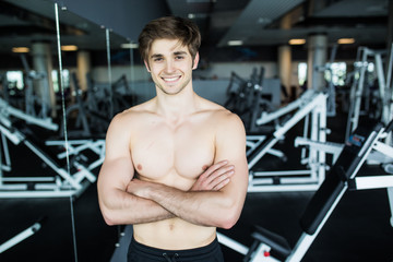 Fototapeta na wymiar Muscular, shirtless young man resting in gym during workout, showing muscular torso, pecs and abs in the mirror at gym