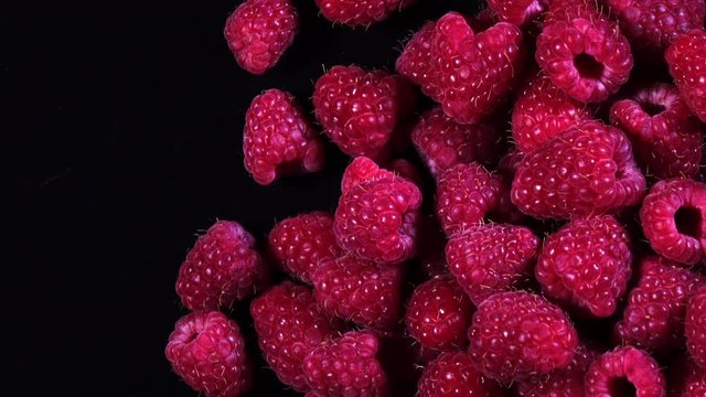 4K top view of ripe juicy raspberries rotating on black background with copy space from the left side.
