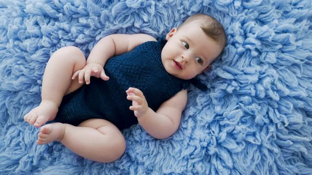 baby in a blue knitted jumpsuit clothes lying on blue fur