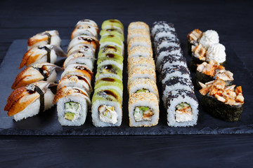 Sushi rolls, maki, nigiri and gunkan set served on black stone slate on dark background
