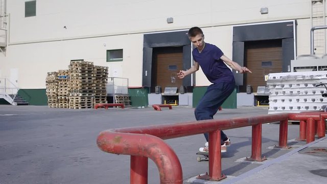 Teenager is jumping and making grind trick on skateboard along red railing in skaterpark. Skateboarder doing nosegrind on funbox outdoors. Boy spending time practicing summer extreme sport.