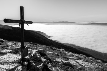 A wooden cross on top of a mountain, with a sea of fog below