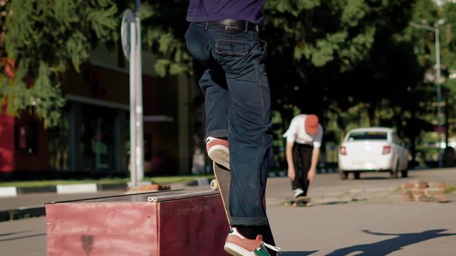 Close up of young skateboarder jumping over the ledge in summer day. Teenager on board sliding on barrier doing nose grind trick. Extreme sport enthusiast sliding on box performing stunt in skatepark.