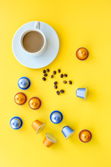 Beverage capsules for coffee mashine near coffee cup and grains on yellow background top view