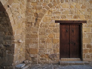 Fototapeta na wymiar Old wooden door in the stone wall, ancient Mediterranean style.