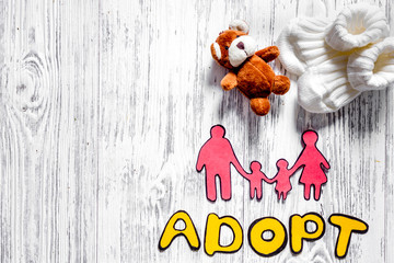 Adopt word, paper silhouette of family and toys on light wooden table background top view copyspace