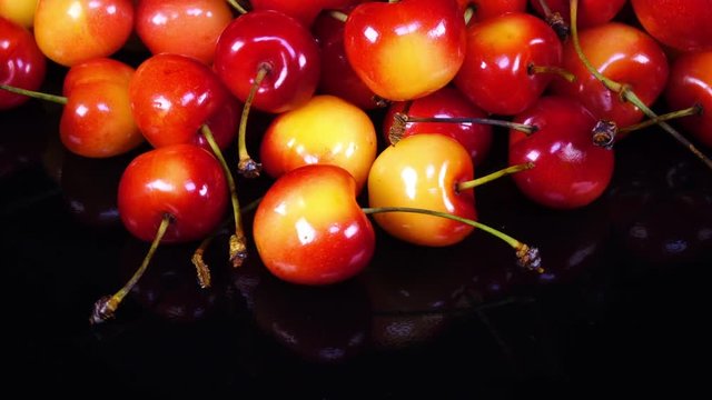 Excellent top view close up of red and yellow fresh sweet cherries with stems, rotating clockwise with up center on black background. Yummy berries with amazing texture in 4k, 3840x2160, clip.
