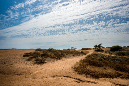 Landscape view with walking trail in Portugal Algarve. Red soil and cloudy sky.