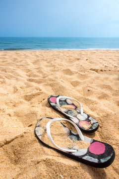 A pair och sandy flip flops on a beautiful summer beach with blue horizon and no people.